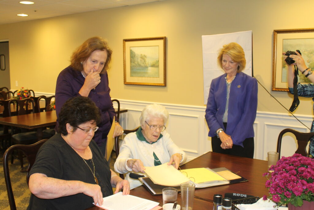 Martha looking at scrapbook with Debbie and Asbury folks look on. 